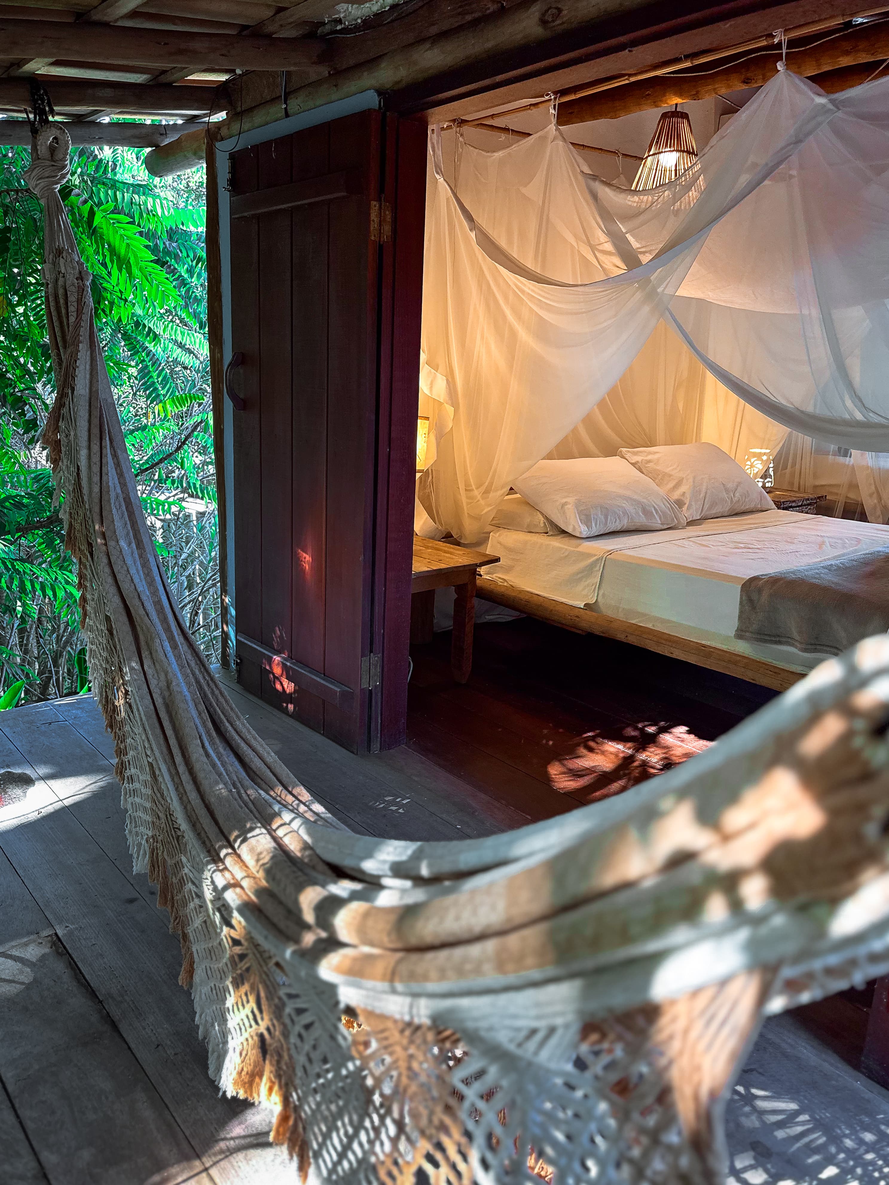 Refúgio em Caraíva ao entardecer — cama com mosquiteiro e rede sob luz dourada